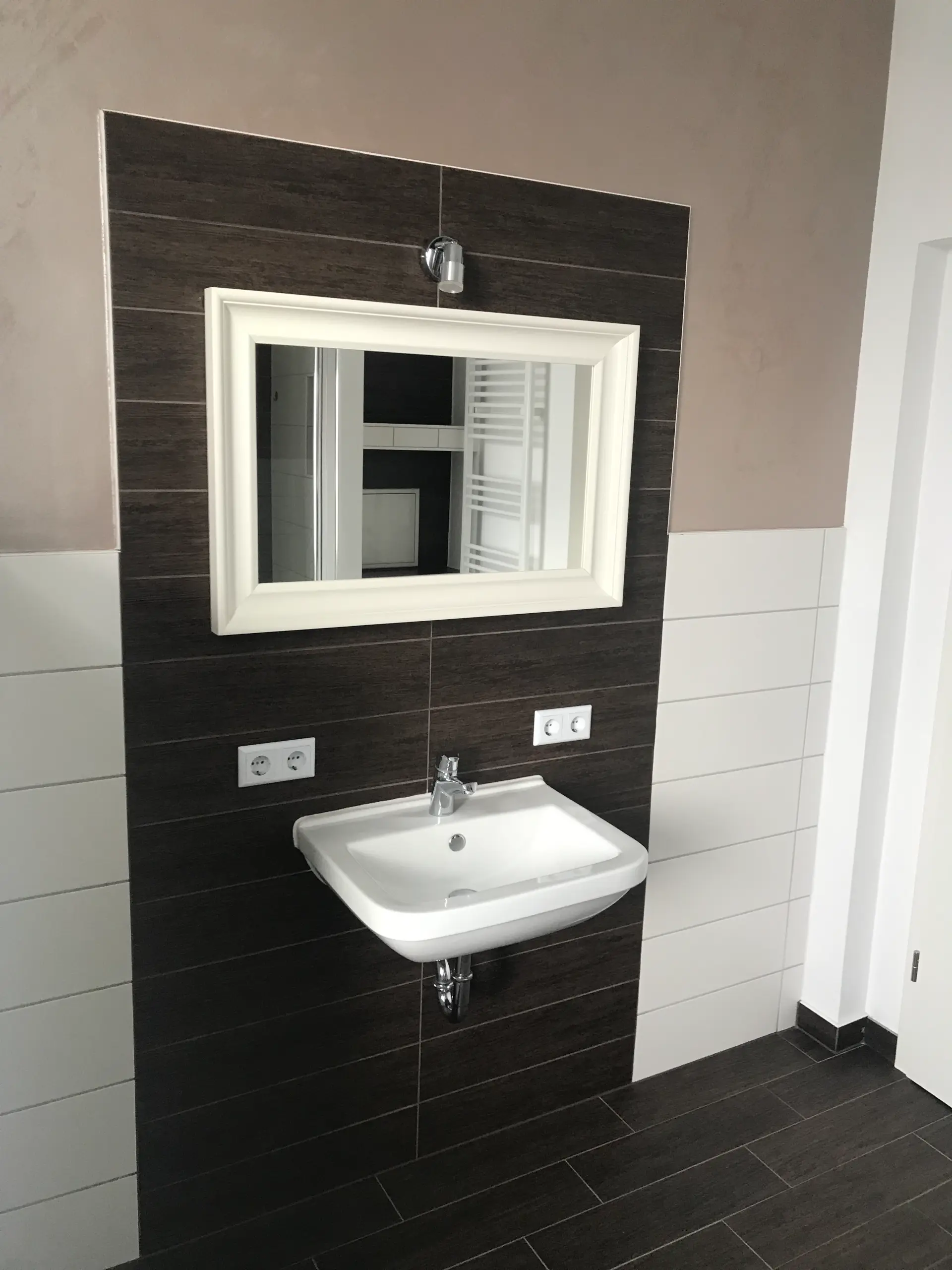 Badezimmer mit Waschbecken, Spiegel und dunklen Fliesen